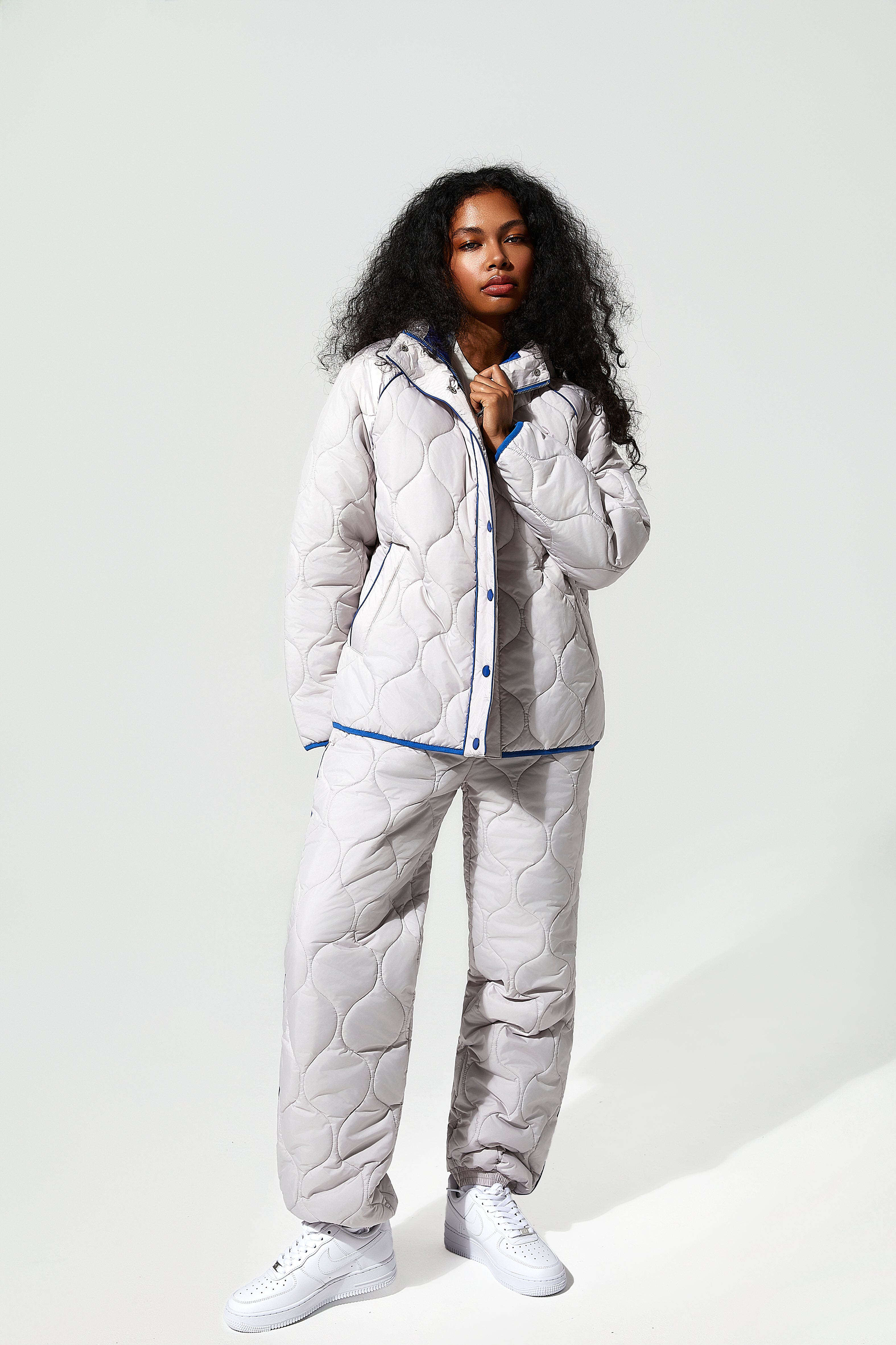 A black model wearing an ice white puffer jacket and quilted trousers with blue detailing