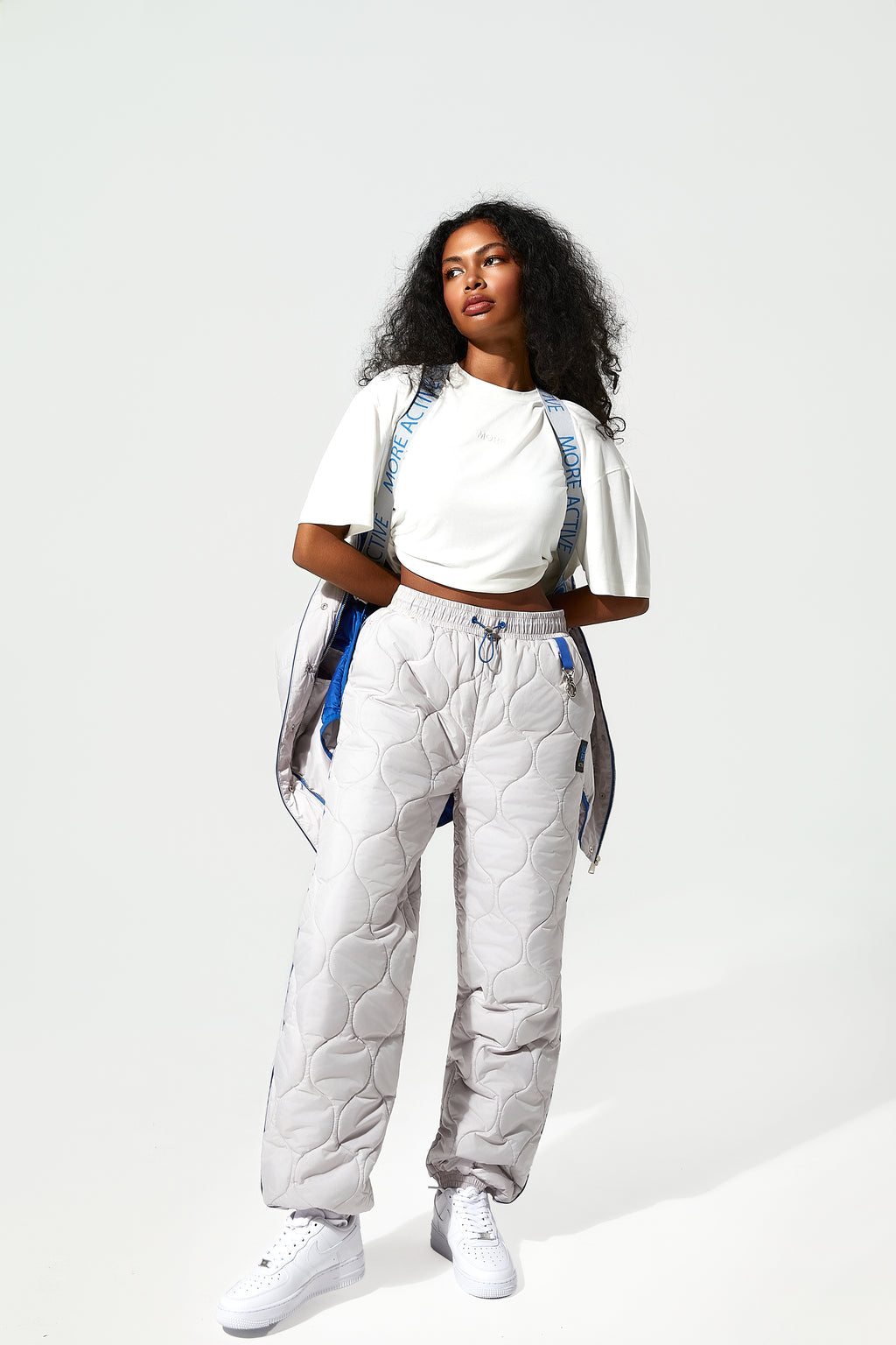A female Model wearing ice white quilted trousers, blue piping details. with  More Active branded suspender straps around the shoulders.