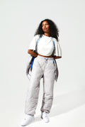 A female Model wearing ice white quilted trousers, blue piping details. with  More Active branded suspender straps around the shoulders.
