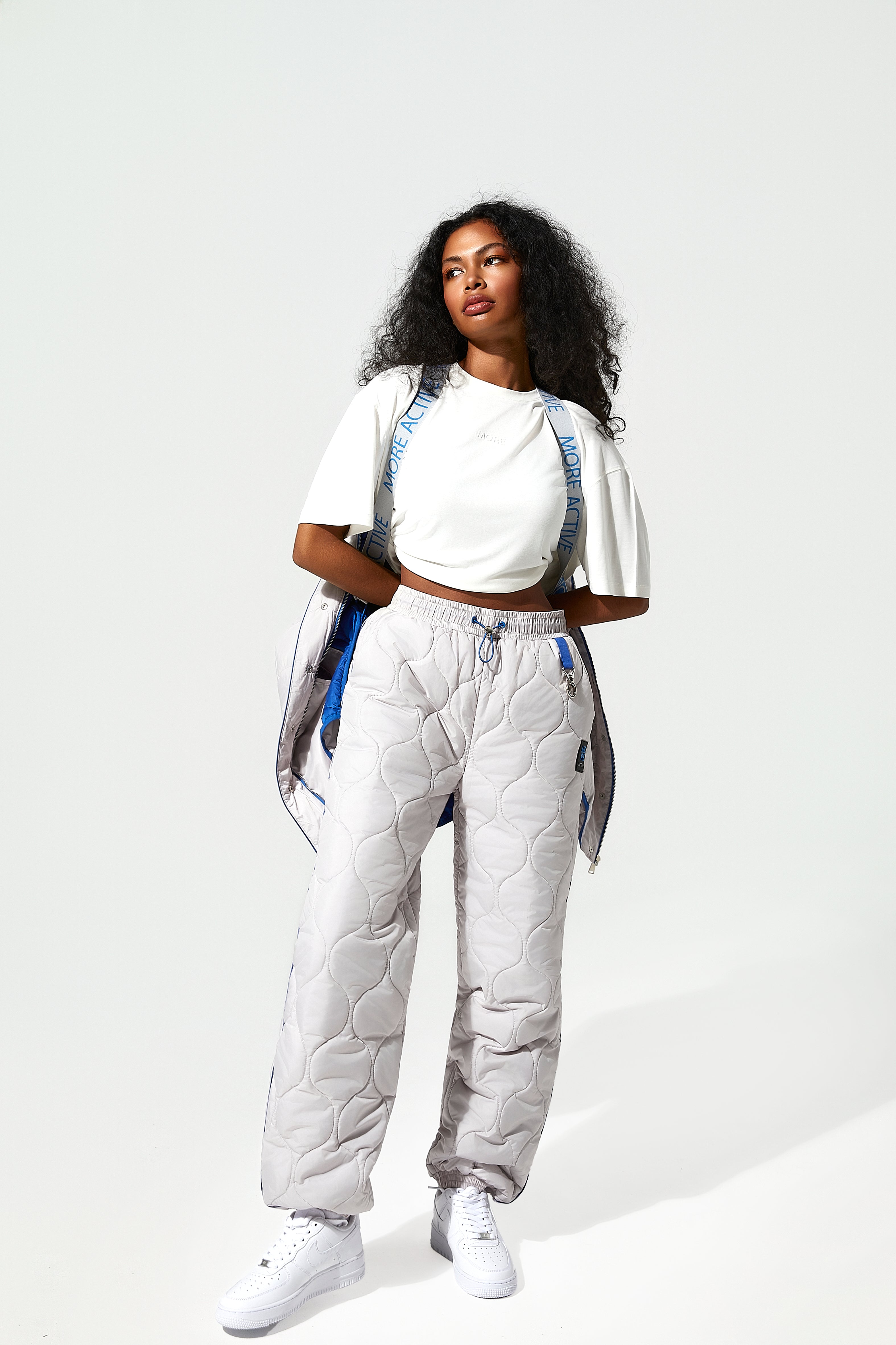 A female Model wearing ice white quilted trousers, blue piping details. with  More Active branded suspender straps around the shoulders.