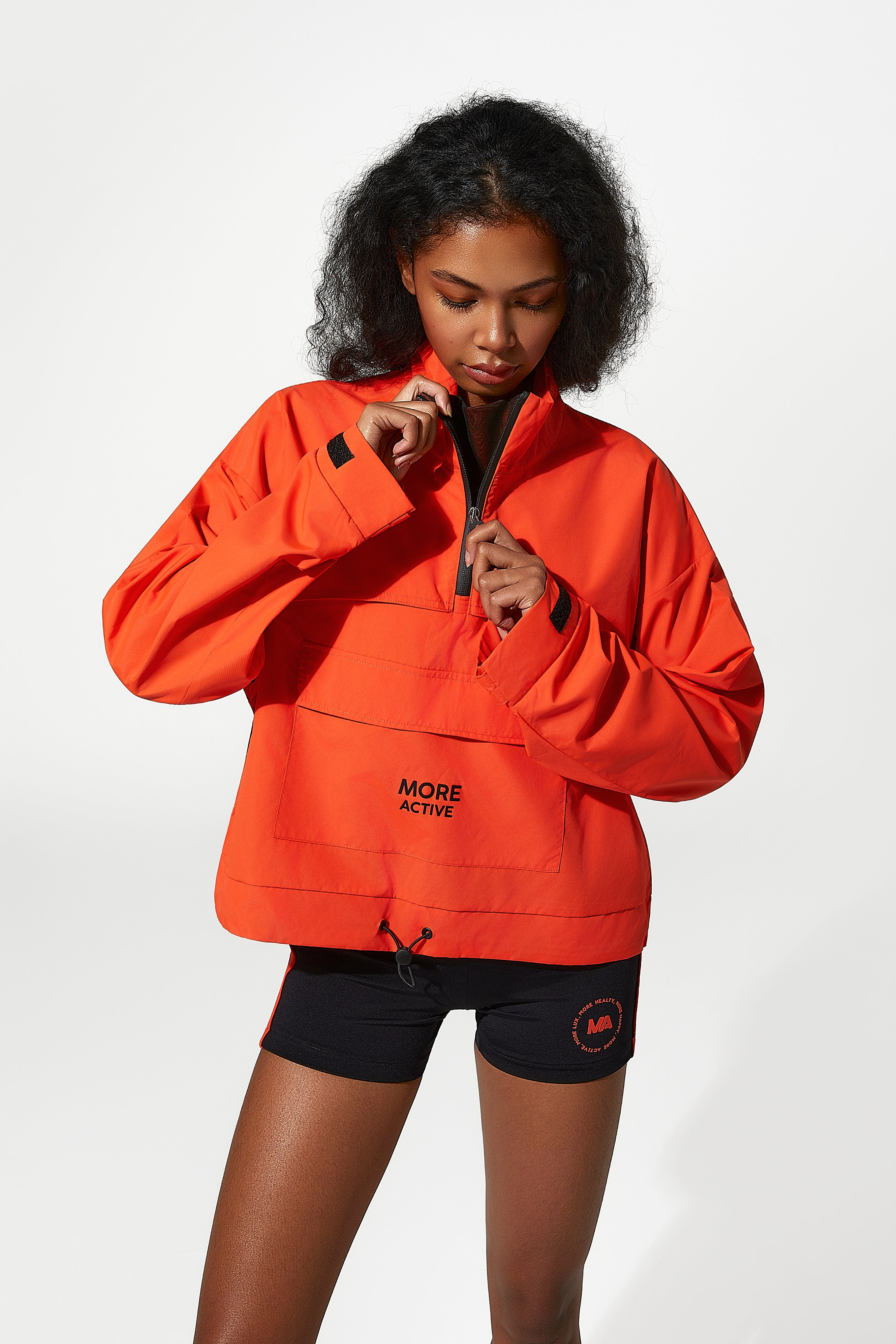 A model  wearing an orange Woman wearing waterproof windbreaker jacket with 'More Active' branding.