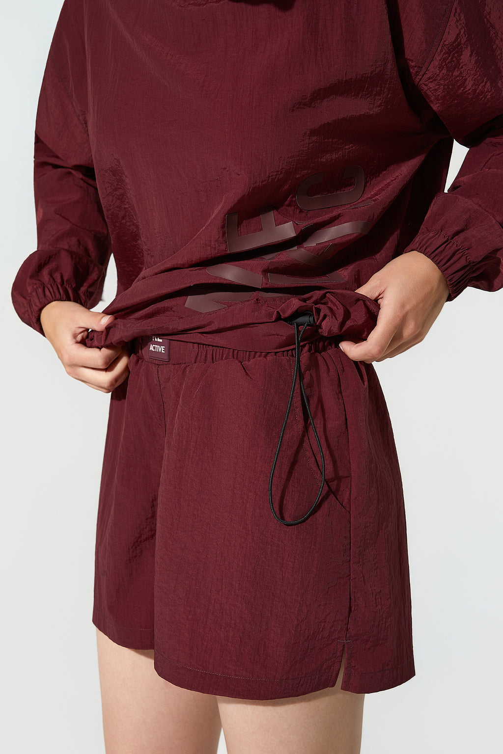 Athletic burgundy windbreakers for women styled with shorts, emphasizing the comfort and versatility of the More Active womens windbreaker.