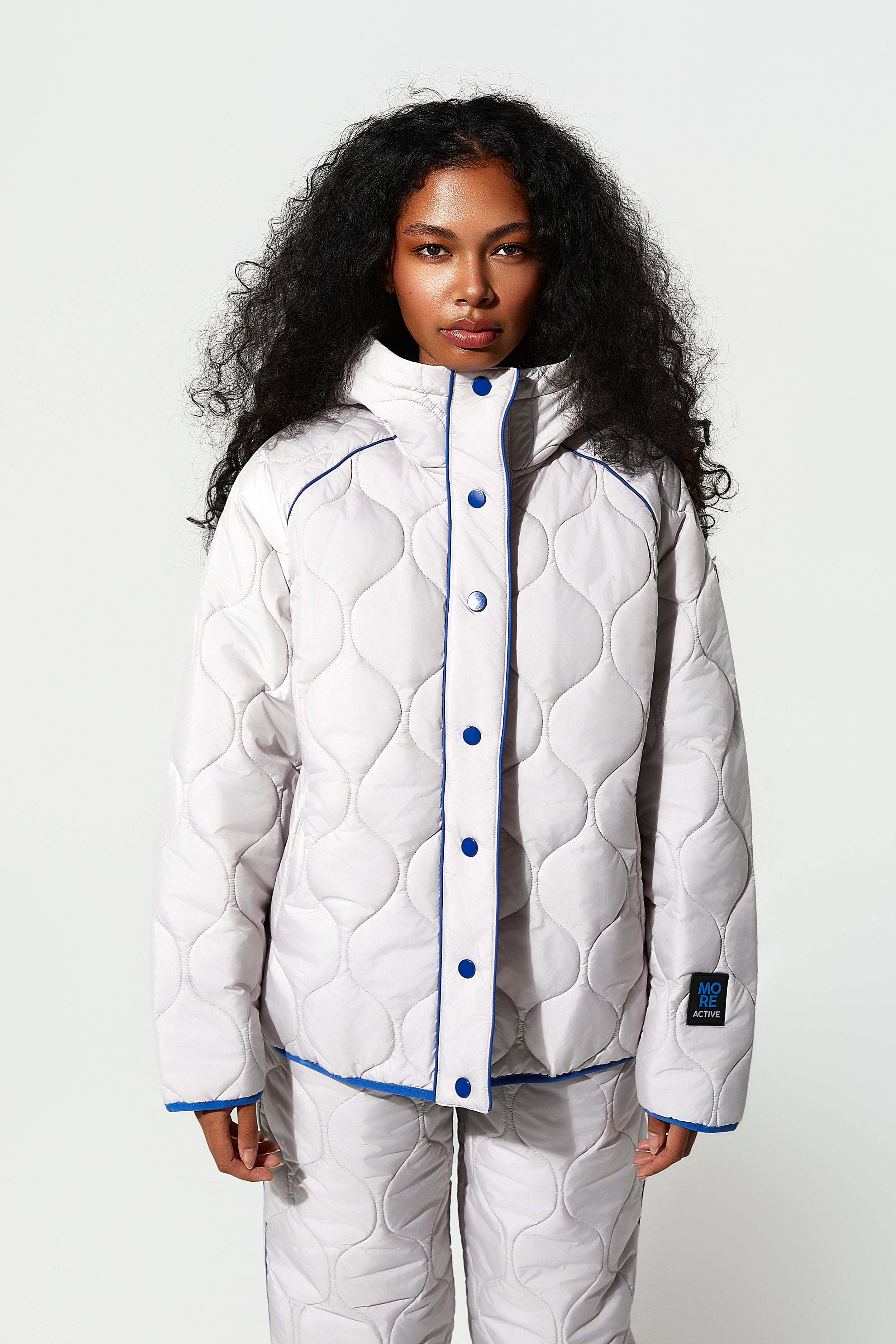 Model  wearing a white quilted jacket with blue buttons on a white background