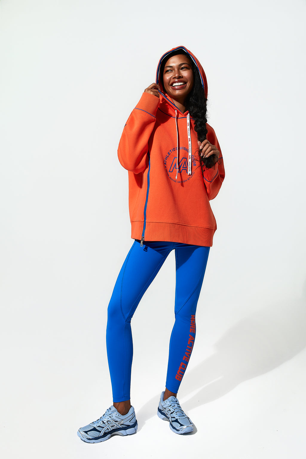 Model wearing an orange womens hoodie and blue leggings on a white background