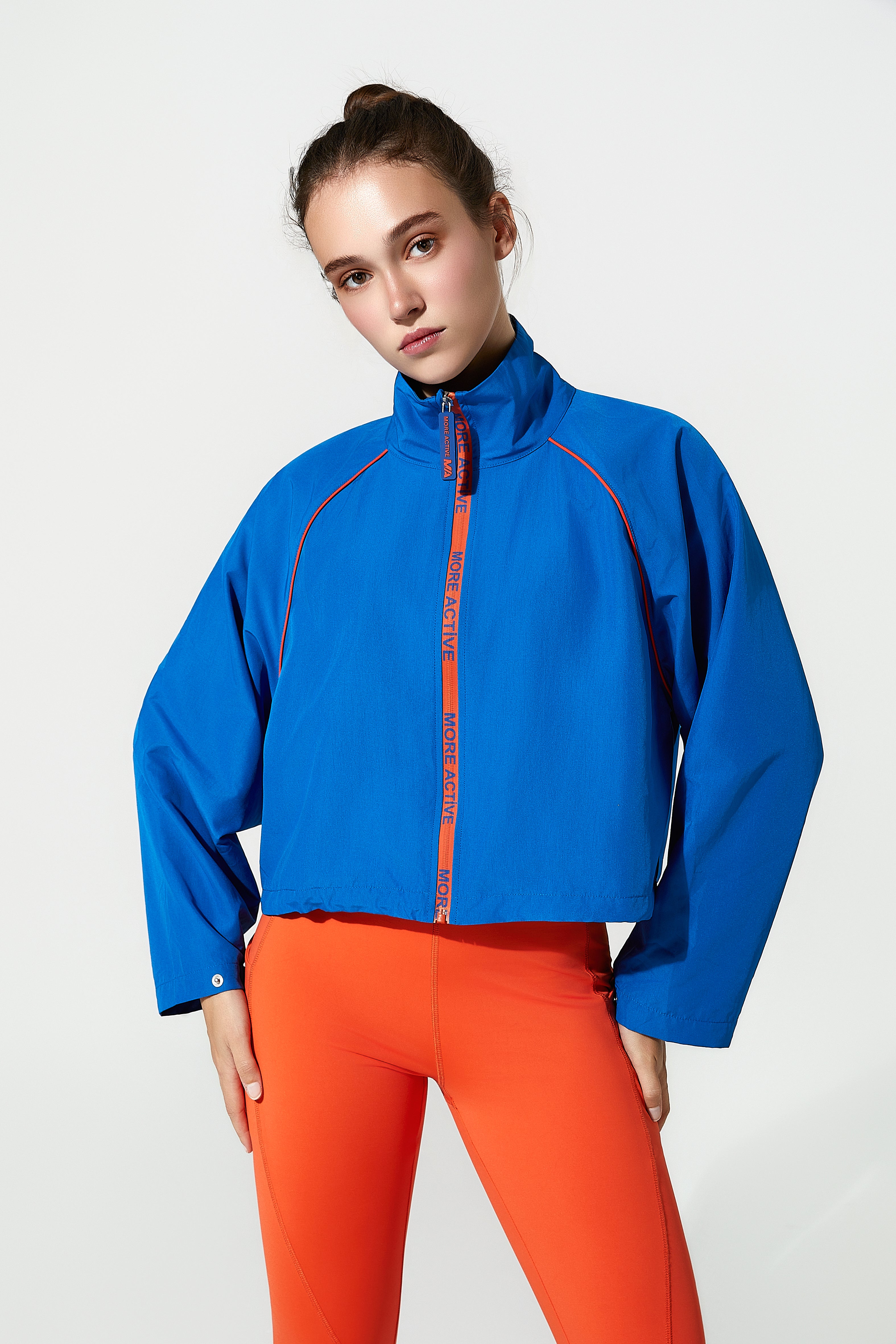 Person wearing a blue cropped jacket with red accents and orange pants on a white background