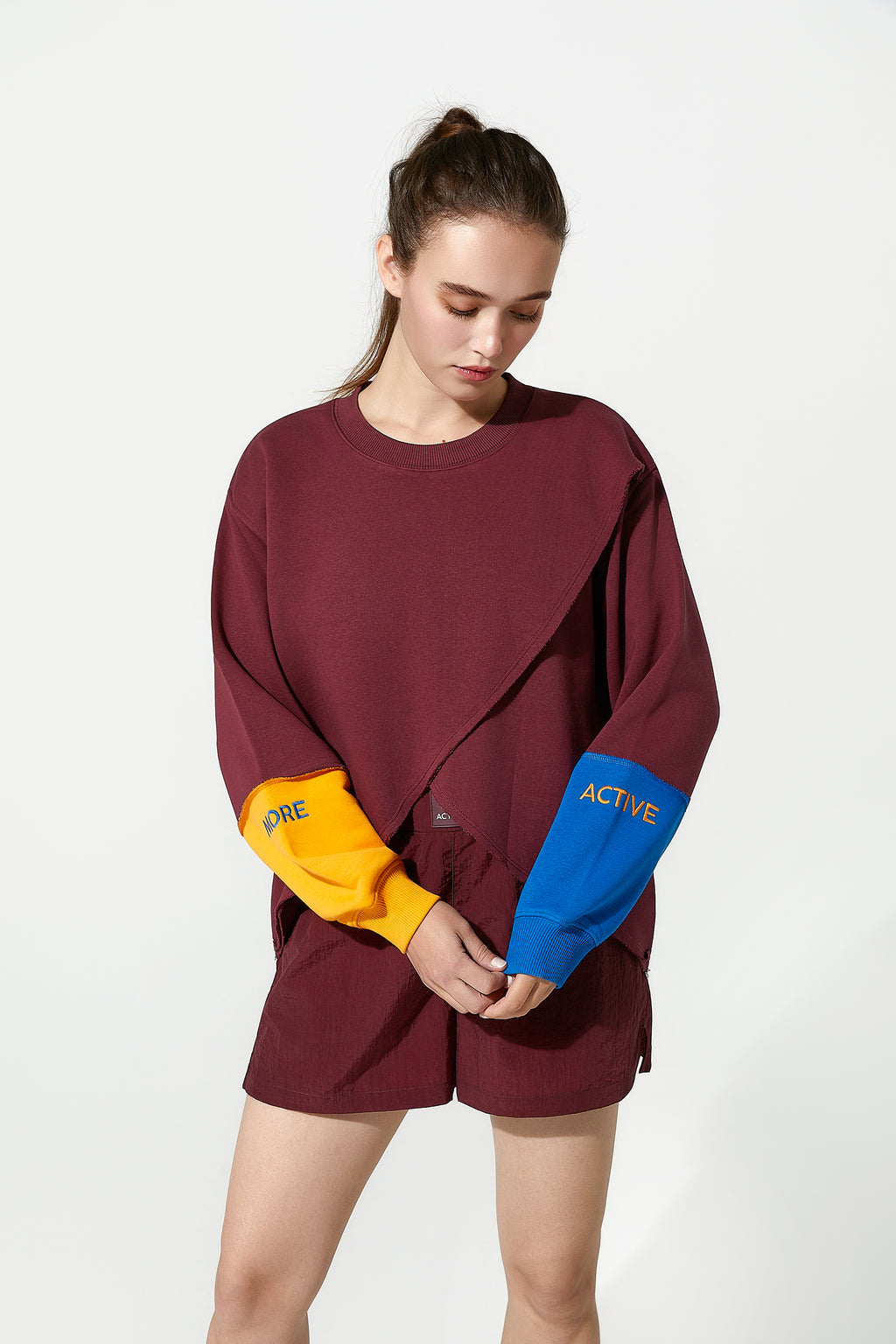 Person wearing a burgundy oversized track top with colourful sleeves on a white background
