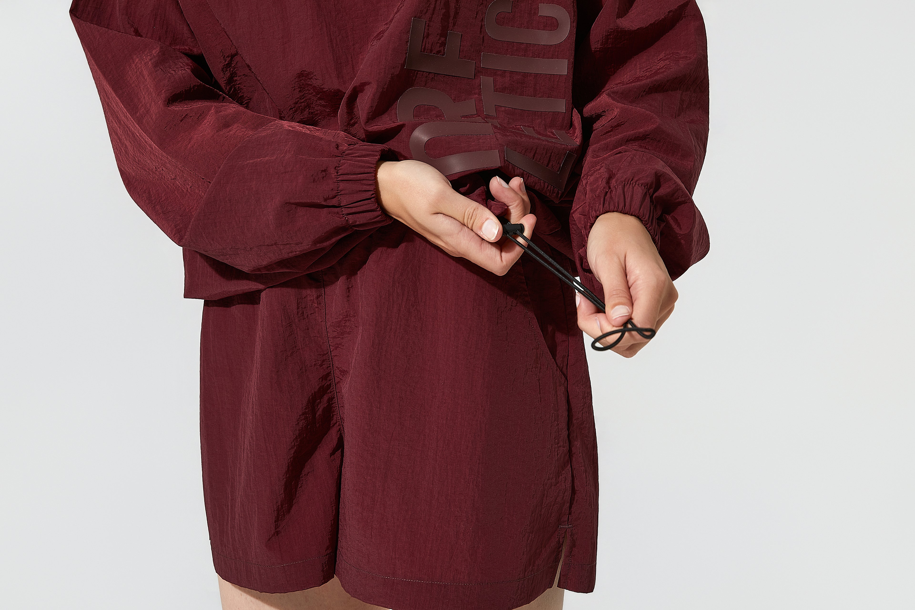 Sleek burgundy windbreakers for women with lightweight sports shorts, presenting the More Active womens windbreaker in a casual standing pose.