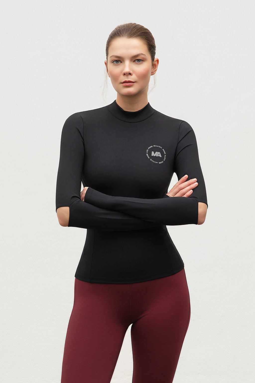 Woman wearing a black long-sleeve  running top with a logo and maroon leggings on.