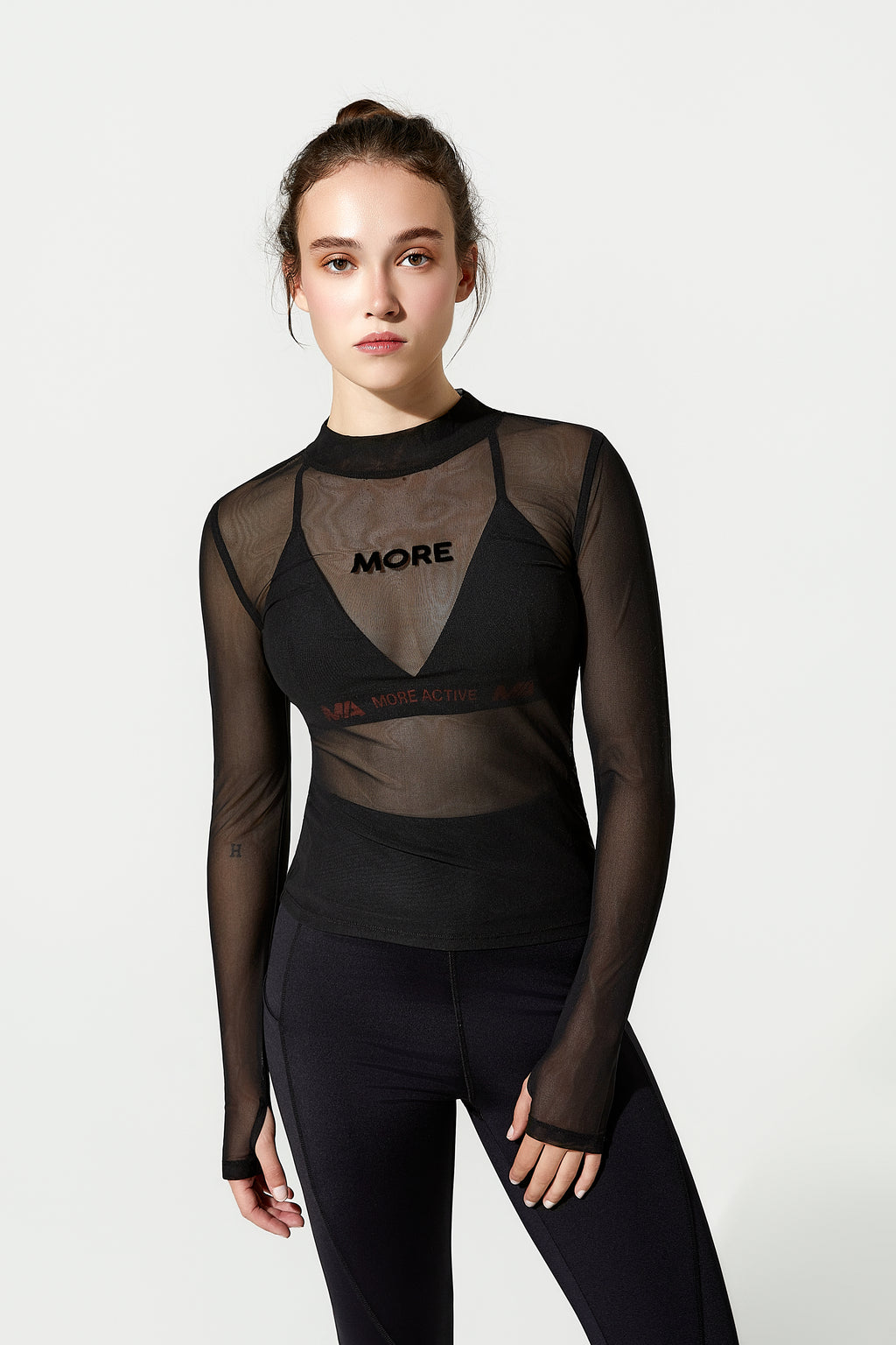 Woman wearing a black sheer long-sleeve gym top with 'MORE' branding 