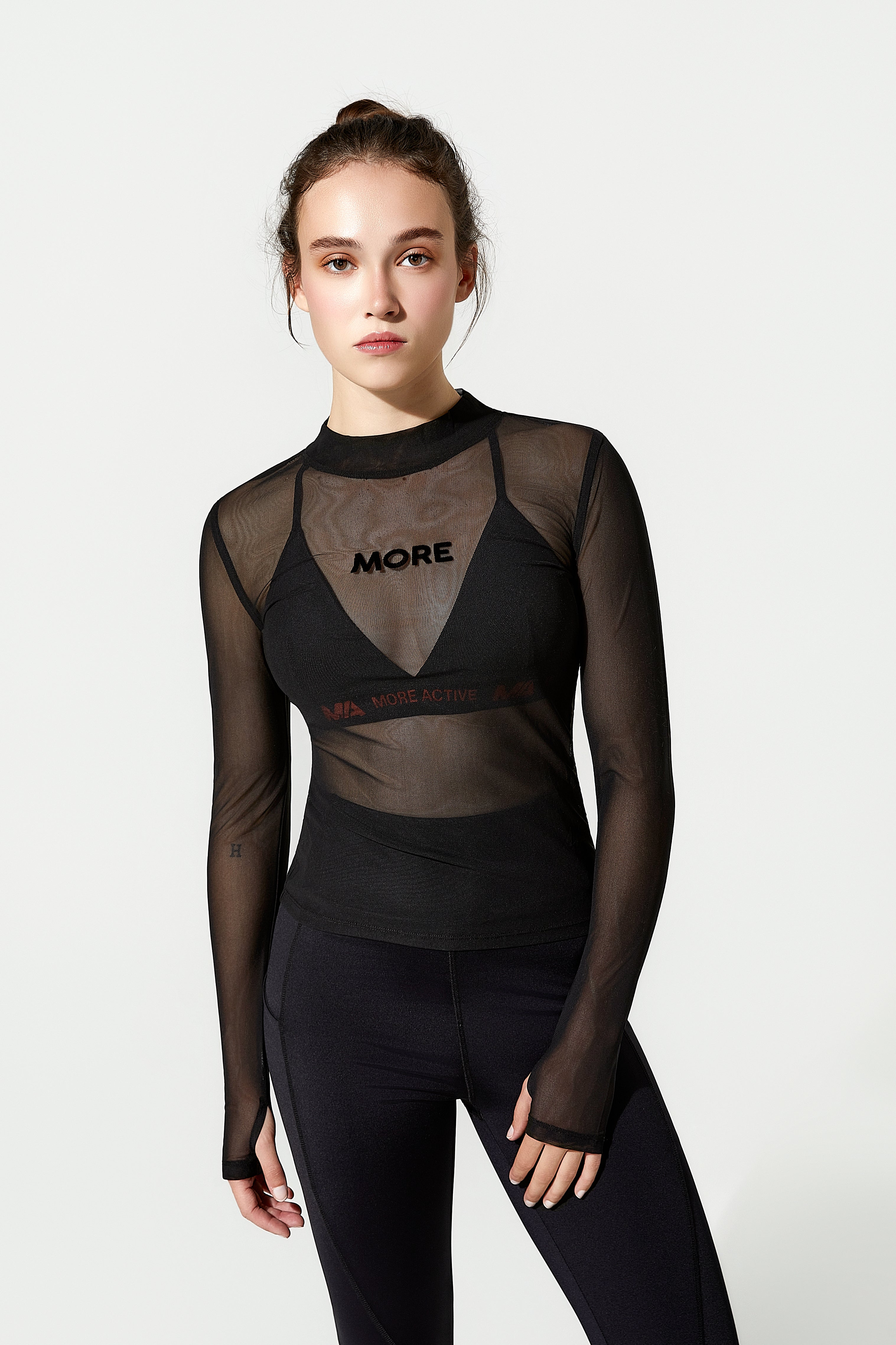 Woman wearing a black sheer long-sleeve gym top with 'MORE' branding 