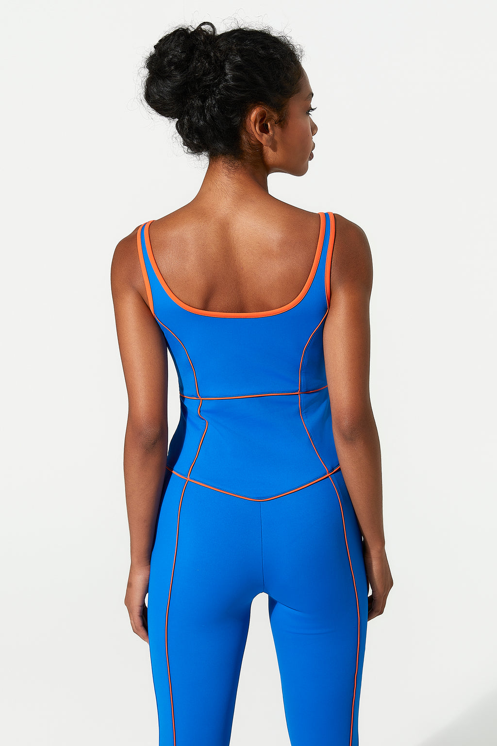 Woman wearing a blue gym jumpsuit with orange accents on a white background