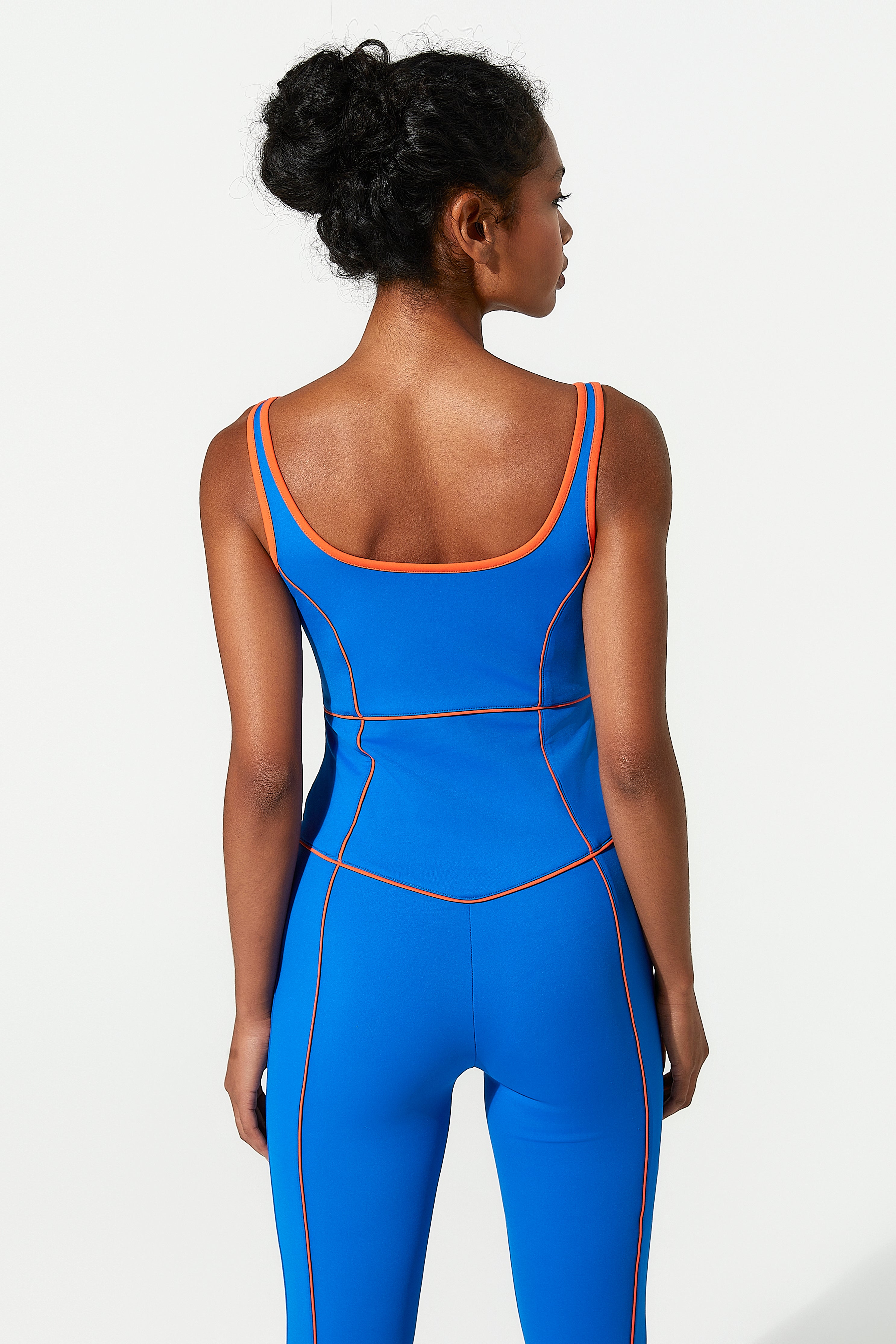 Woman wearing a blue gym jumpsuit with orange accents on a white background