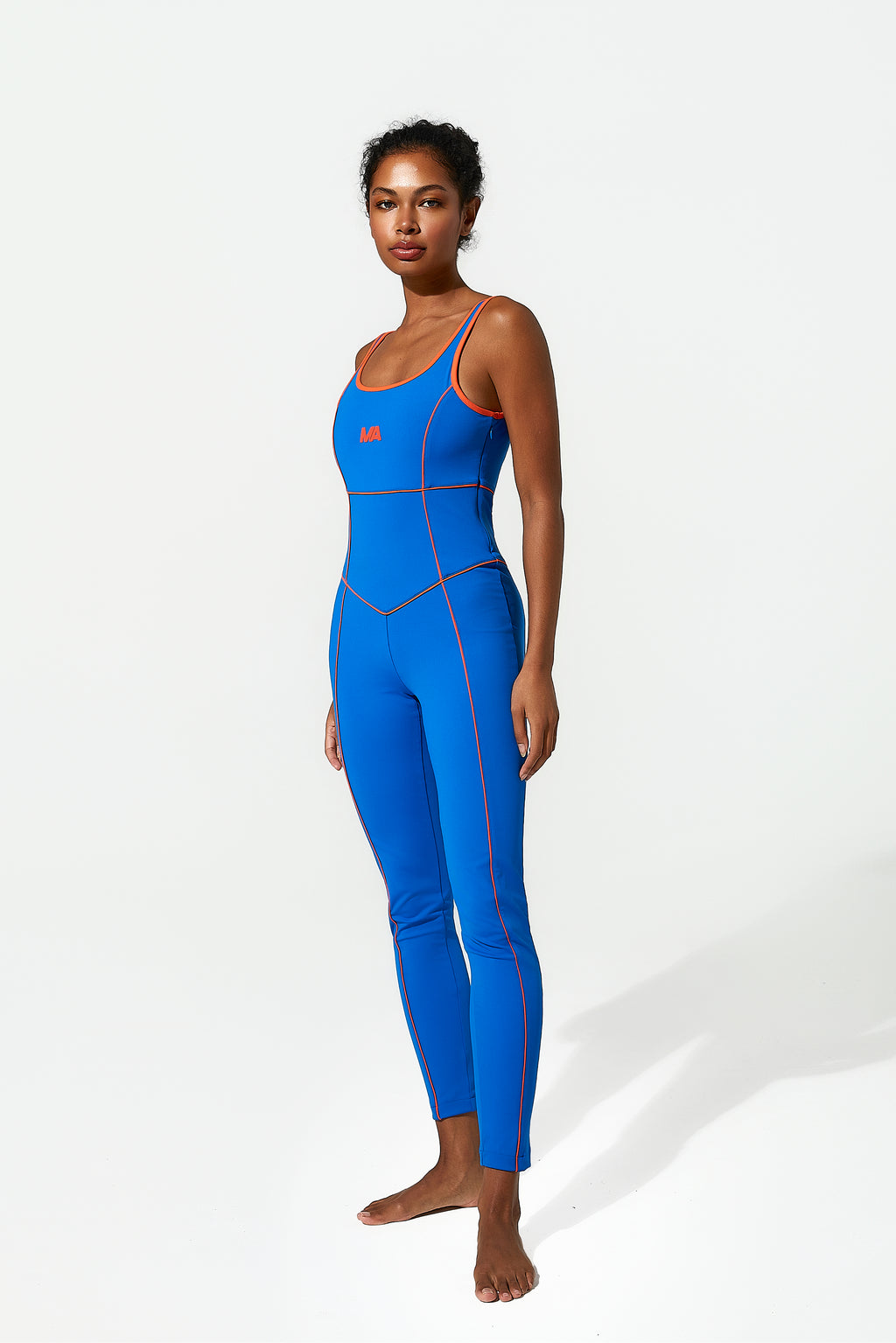 Woman wearing a blue unitard with red piping on a white background
