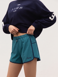 Person wearing a navy sweatshirt with white designs and teal shorts on a light gray background