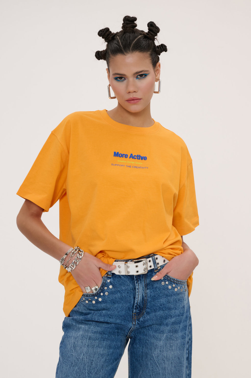 Woman wearing an orange t-shirt with text and blue jeans on a plain background
