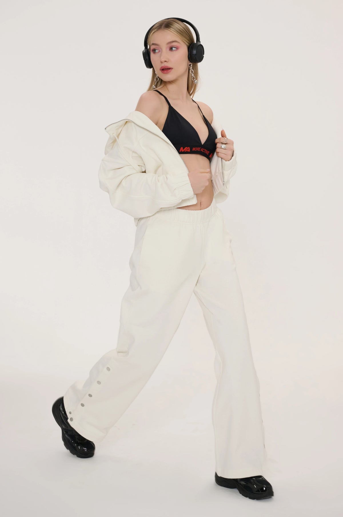 wearing a black bra and white pants with a white jacket 