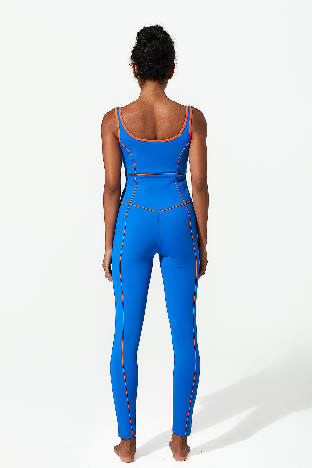 behind shot of a girl wearing a blue jumpsuit with orange accents on a white background