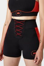 Black athletic shorts with red side panels and red lace-up front detail, shown on a model against a light gray studio background.