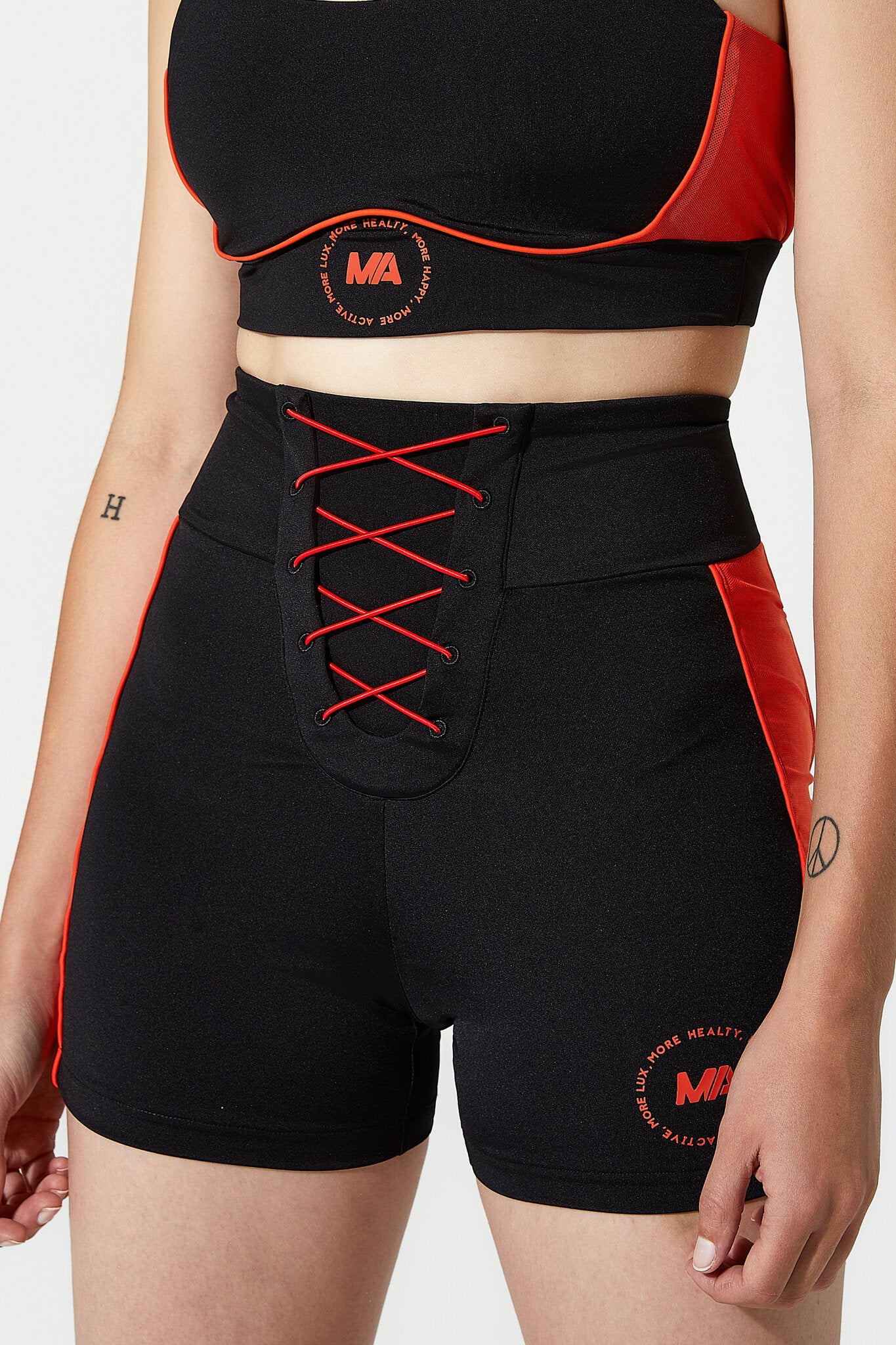 Black athletic shorts with red side panels and red lace-up front detail, shown on a model against a light gray studio background.