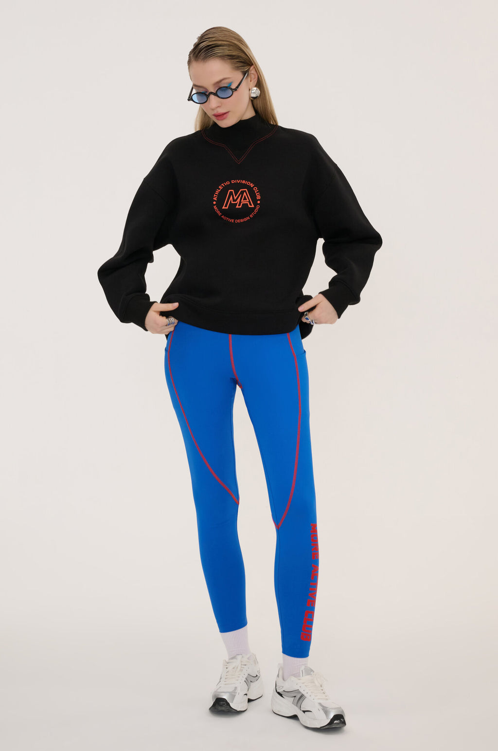 Person wearing a black sweater with a logo and blue leggings on a white background