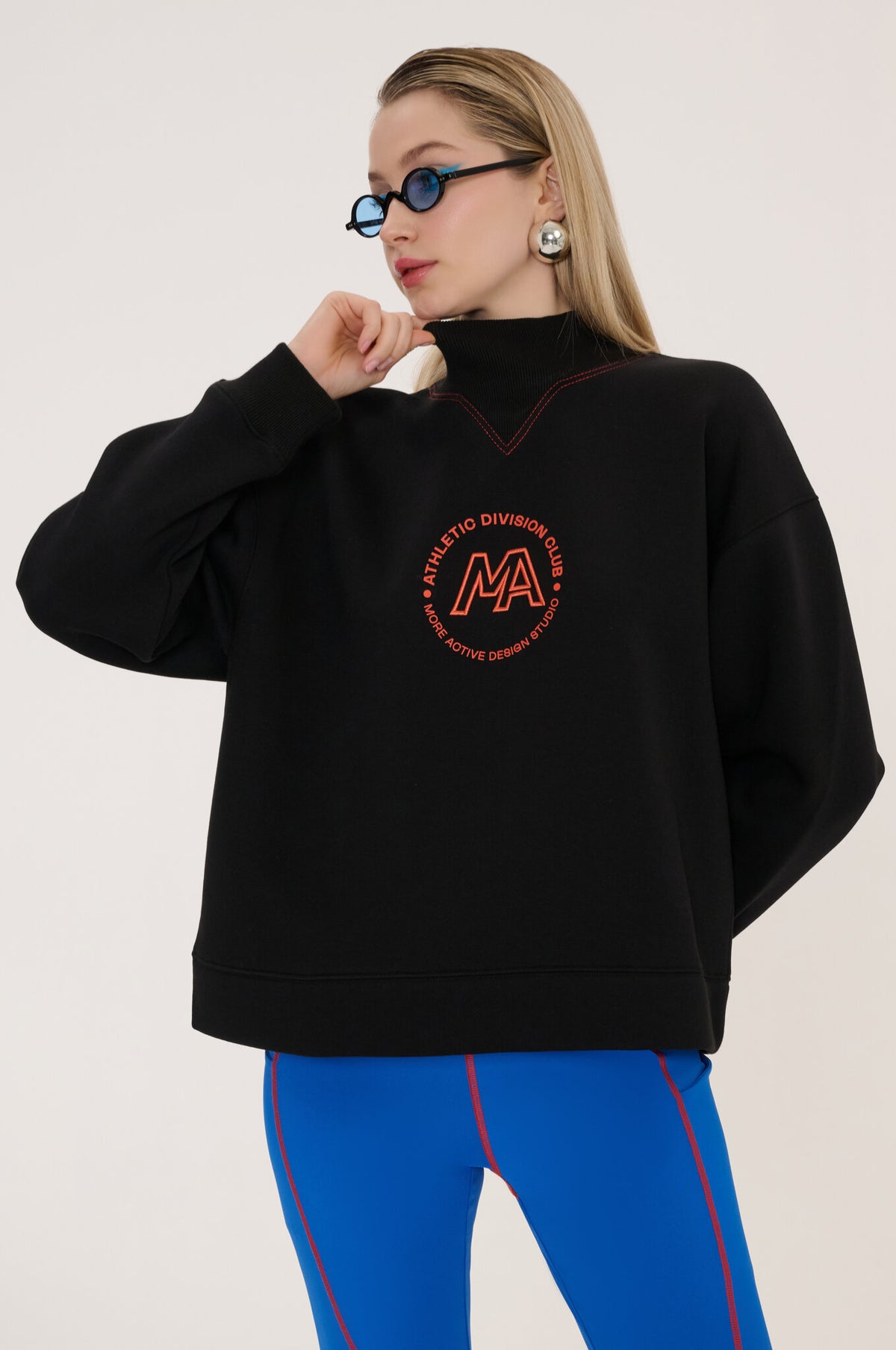 Person wearing a black sweatshirt with a red logo and blue pants on a light background