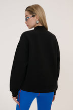 Person wearing a black jacket and blue pants on a plain background
