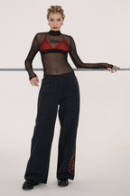 Person wearing a black sheer top with red accents and black wide-leg pants on a white background
