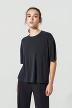A woman modeling a dark navy blue short-sleeve crewneck t-shirt and matching dark pants against a light gray studio background.