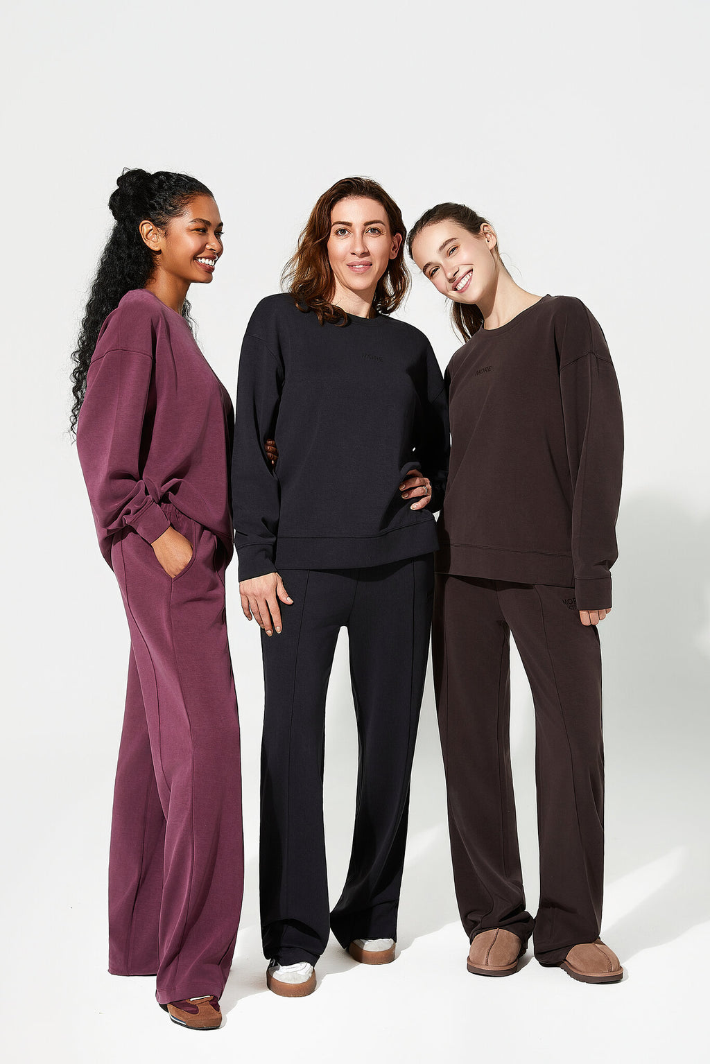 Three women wearing matching outfits in burgundy, black, and brown on a white background