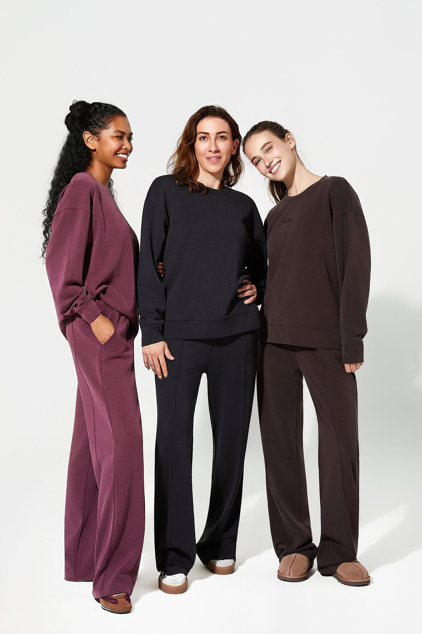 Three women wearing matching outfits in burgundy, black, and brown on a white background
