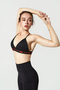 Woman wearing a black sports bra and leggings with red accents on a light gray background