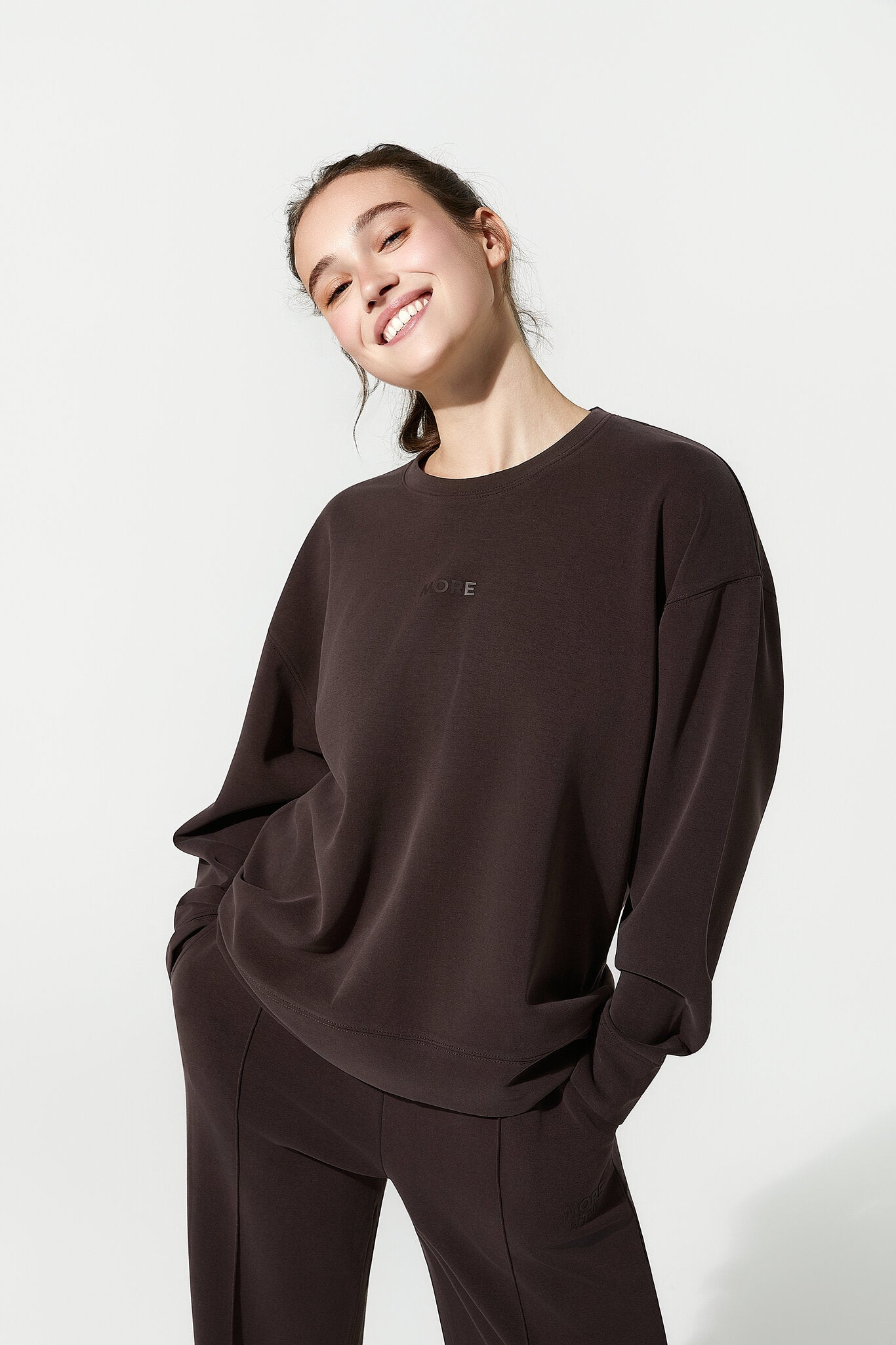 Person wearing a brown sweatshirt and pants on a white background