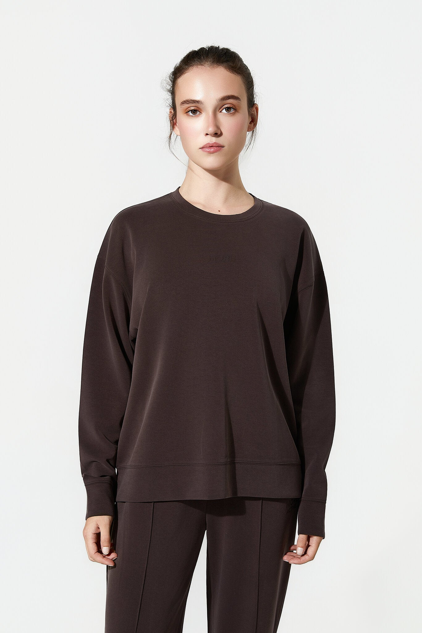 Person wearing a brown long-sleeve top and pants on a white background