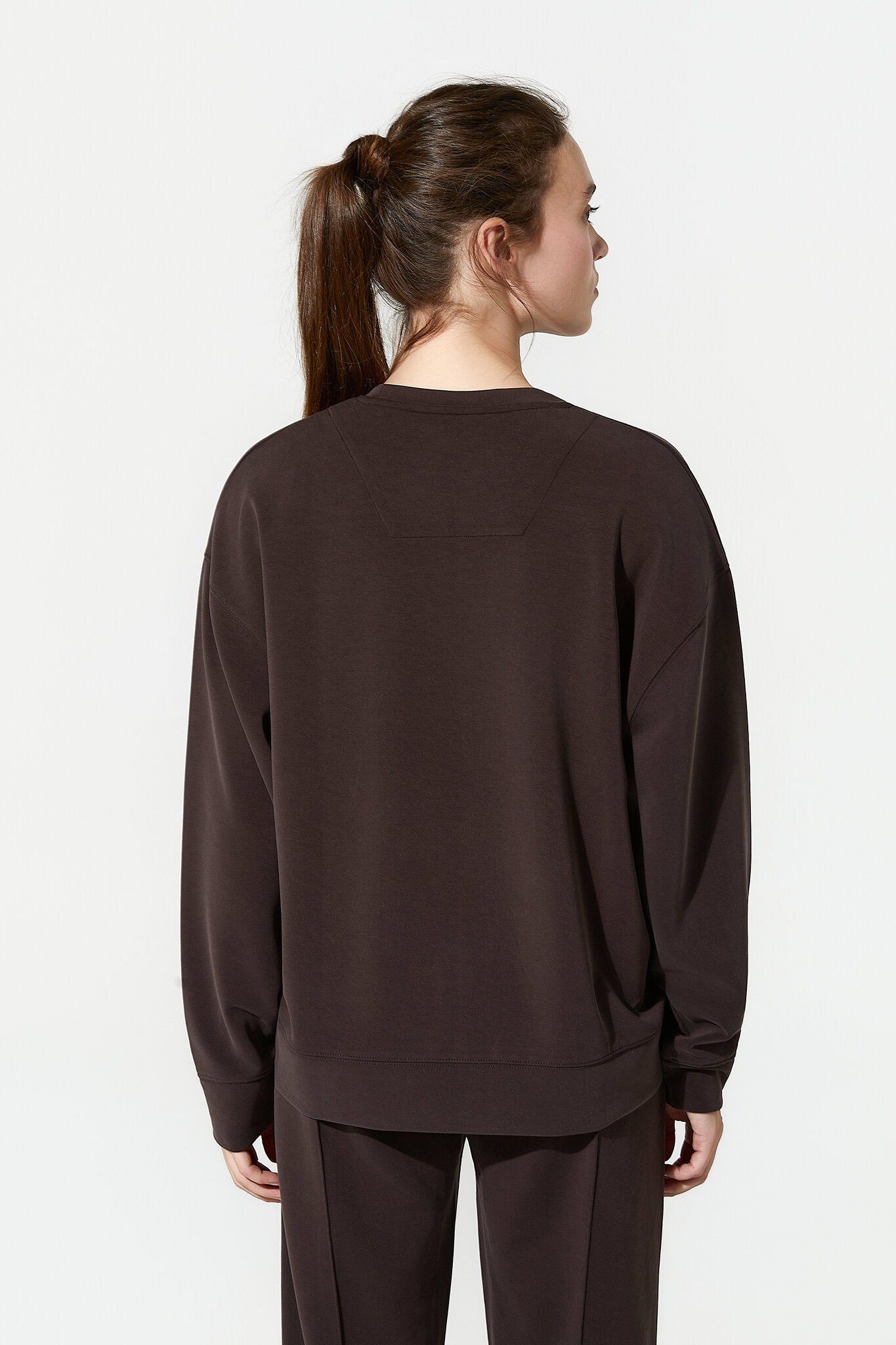 Person wearing a brown sweatshirt and pants on a white background