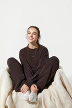 Person wearing a dark brown outfit sitting on a white surface with a beige blanket.