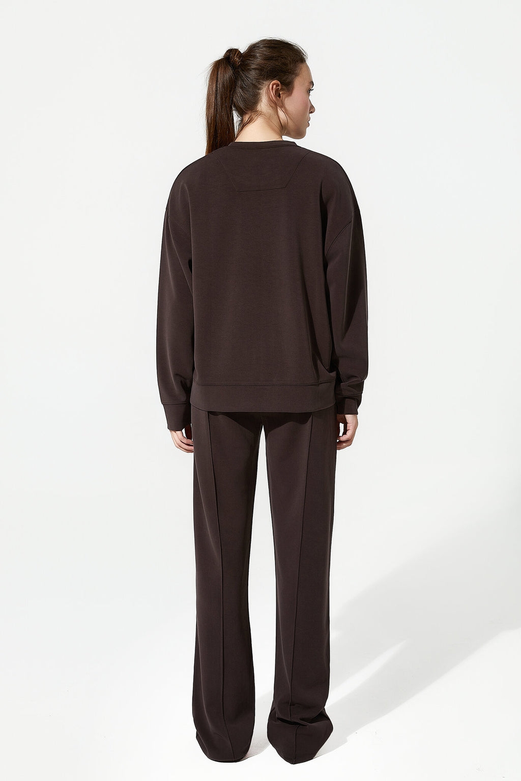 Person wearing a brown sweatshirt and pants on a white background