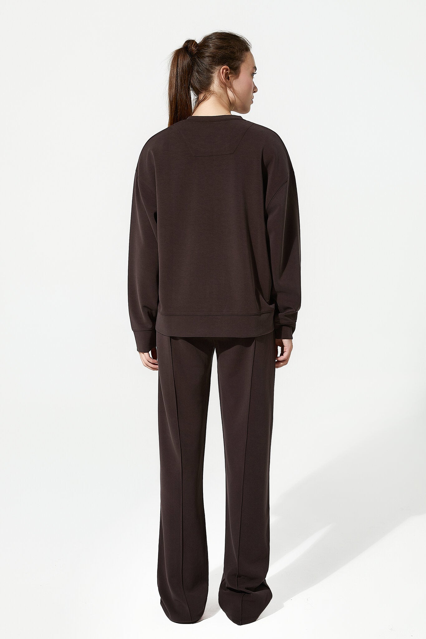 Person wearing a brown sweatshirt and pants on a white background