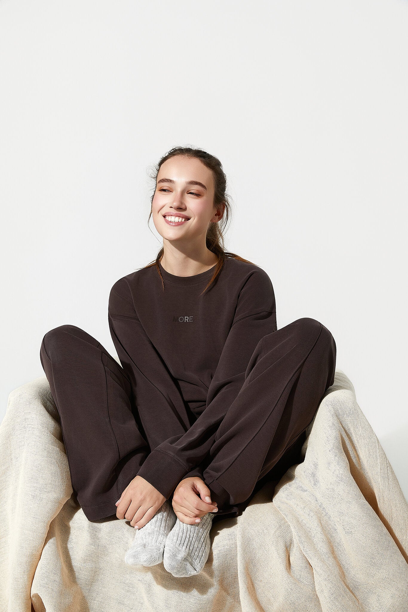 Person wearing a dark brown outfit sitting on a white surface with a beige blanket.