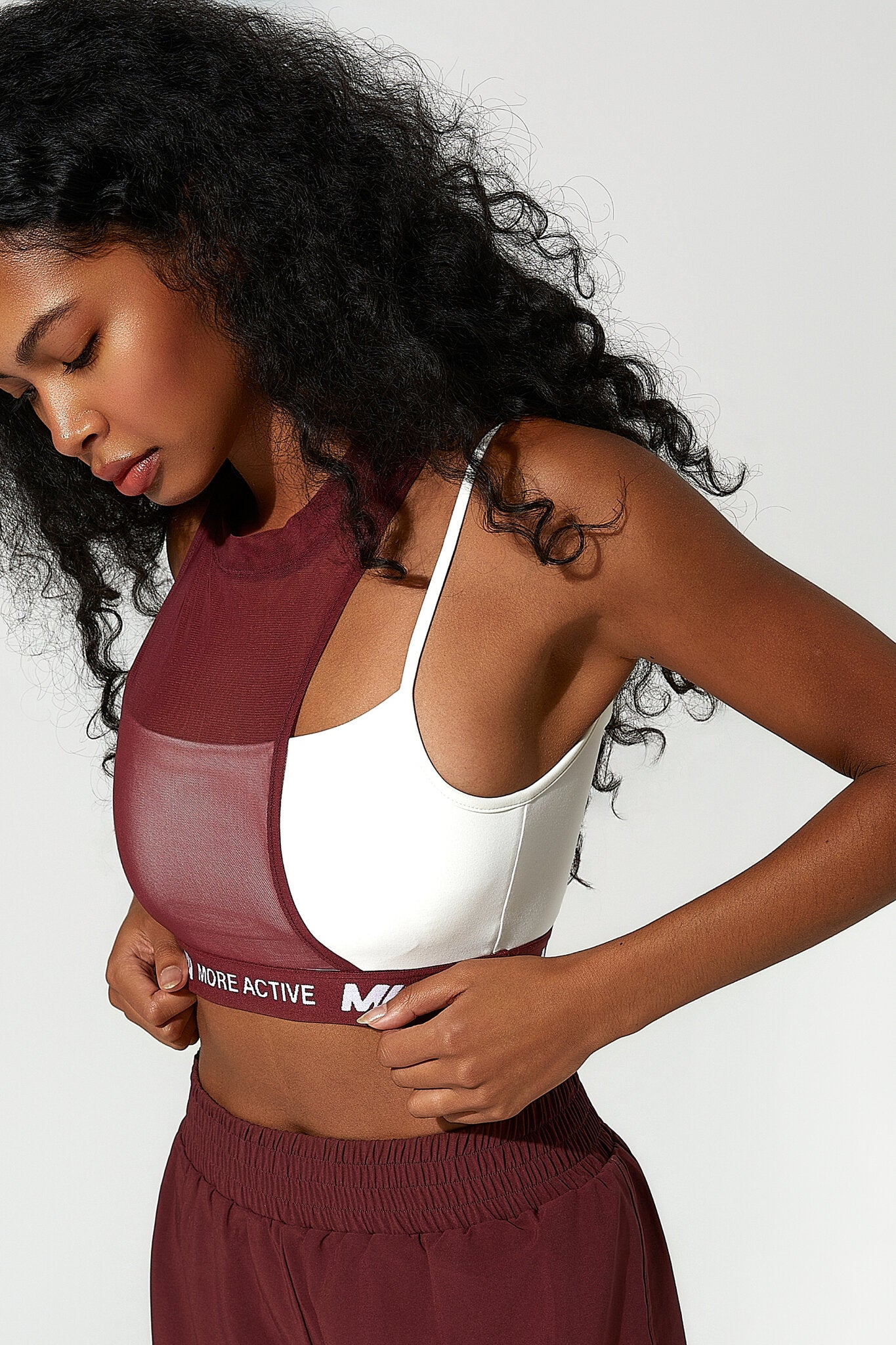 A woman wearing a burgundy and white sports bra with matching athletic bottoms, shown in a close-up studio shot against a light gray background.