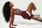 Woman in maroon athletic outfit performing a push-up on a white background