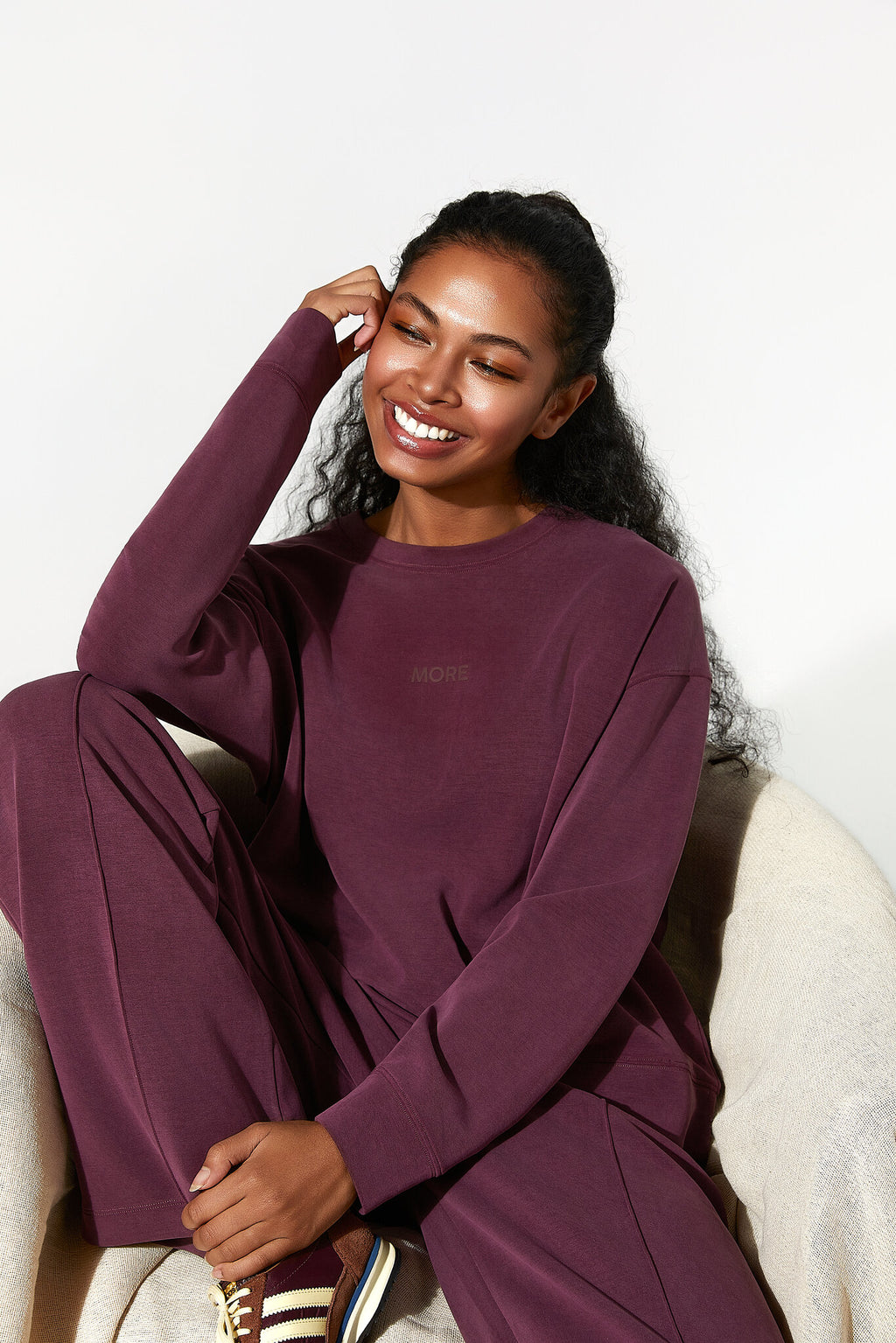 Woman in a burgundy outfit sitting on a white chair against a white background