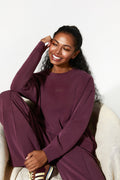 Woman in a burgundy outfit sitting on a white chair against a white background