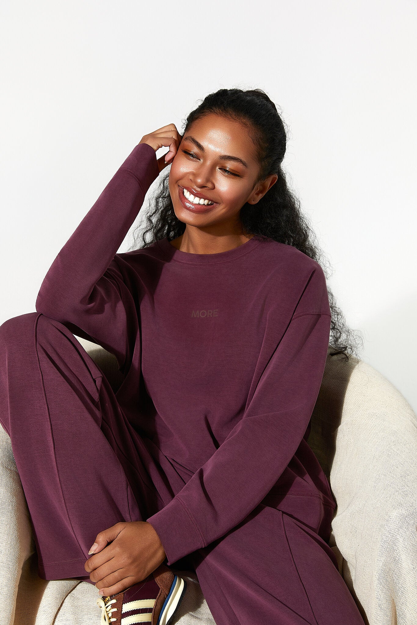Woman in a burgundy outfit sitting on a white chair against a white background