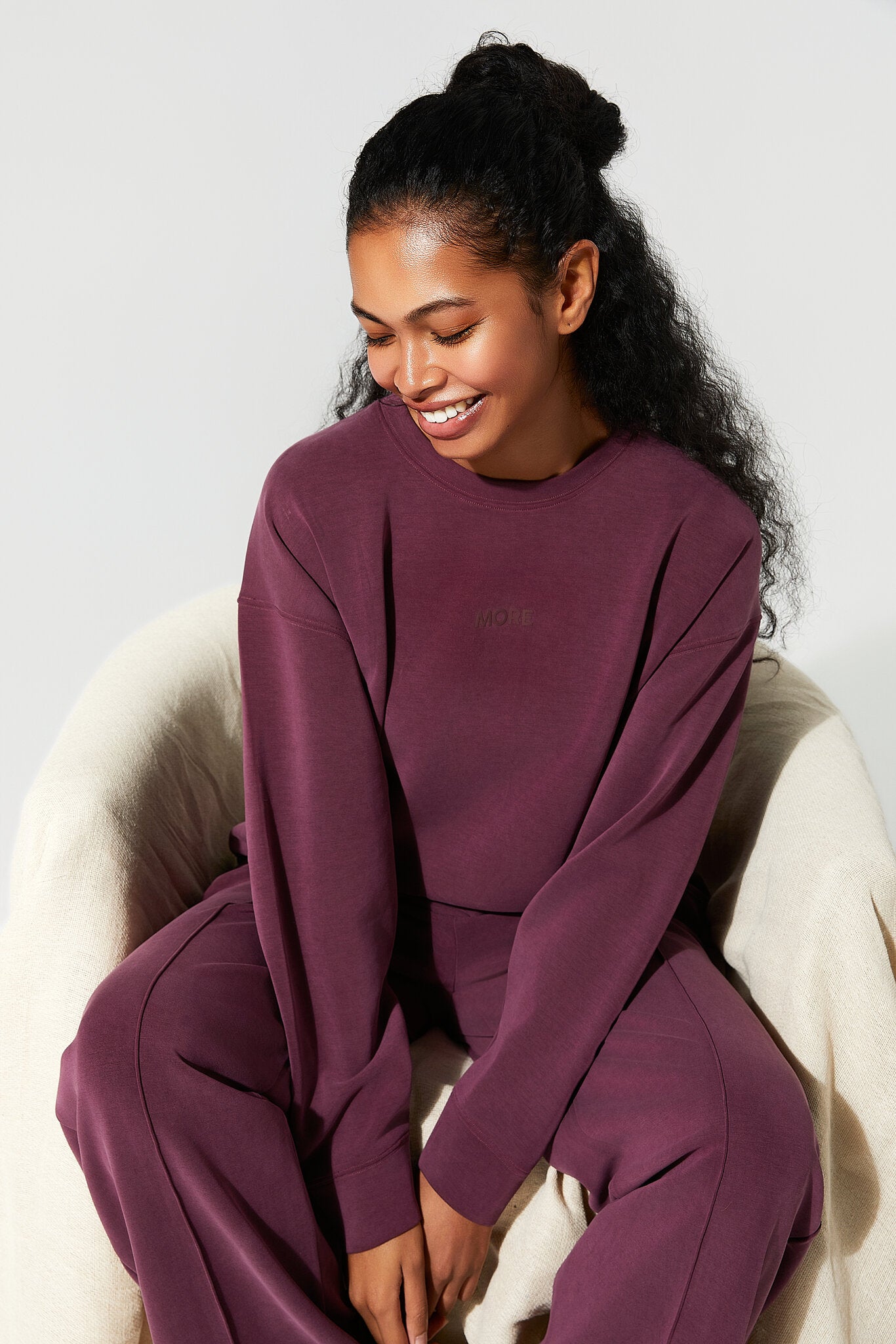 Woman wearing a burgundy outfit sitting on a white chair against a light gray background