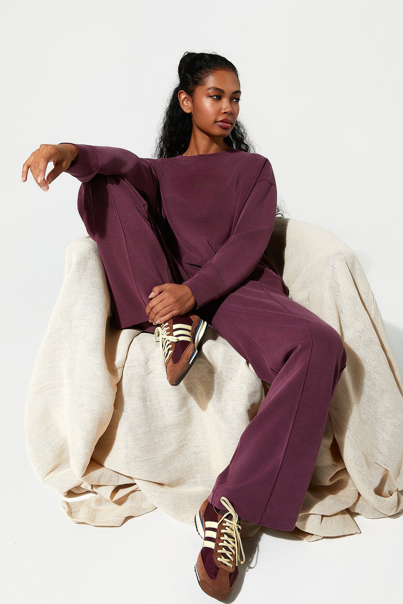 Person wearing a burgundy outfit with Adidas shoes sitting on a white chair.
