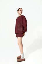 Person wearing a burgundy oversized sweatshirt and shorts set on a white background