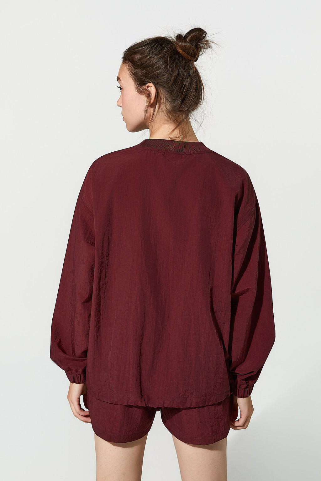 A woman shown from the back wearing a loose-fitting burgundy long-sleeve top and matching shorts against a plain light gray studio background.