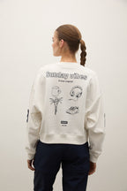 Person wearing a light gray sweatshirt with 'Sunday vibes' text and graphics on the back, standing against a plain background.
