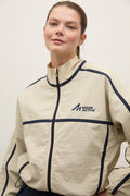 A woman wearing a beige zip-up athletic jacket with navy blue piping and a 'MORE ACTIVE' logo on the chest, photographed against a plain light background.