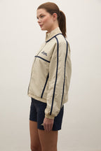 Woman wearing a beige jacket with navy accents on a plain background